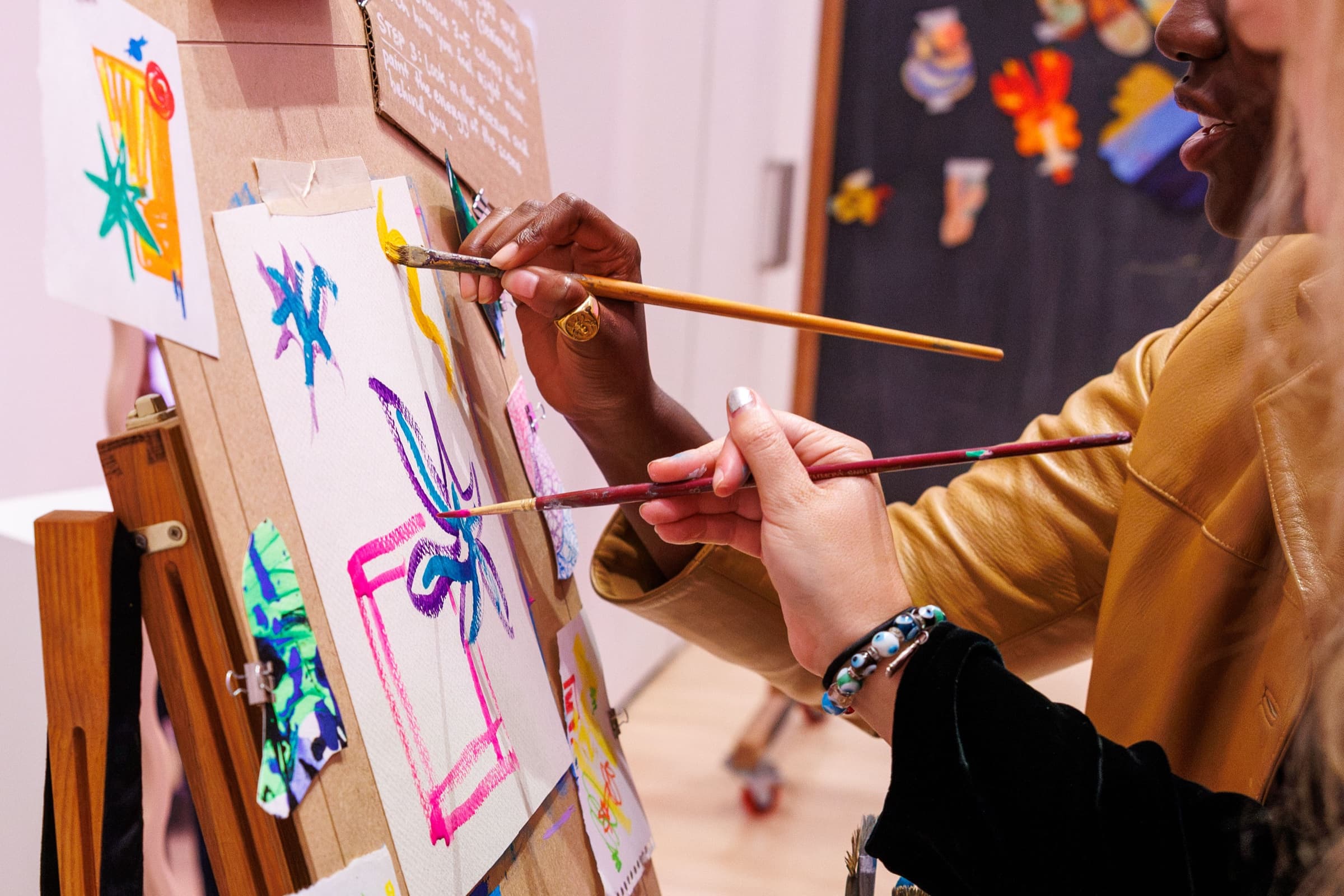 Two people painting together on the same canvas at an easel during Bad Art Club at SFMOMA